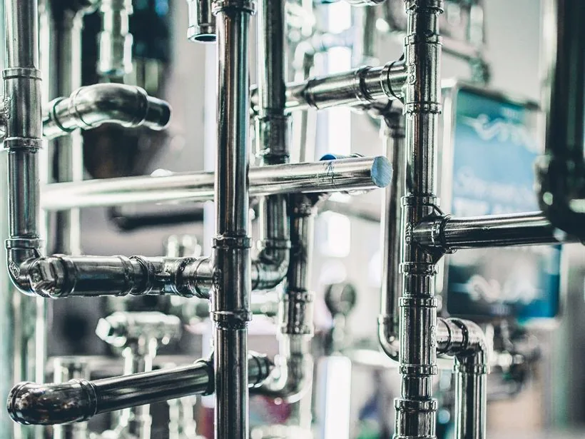 Rede densa de tubulação em aço inox dentro de uma planta industrial.